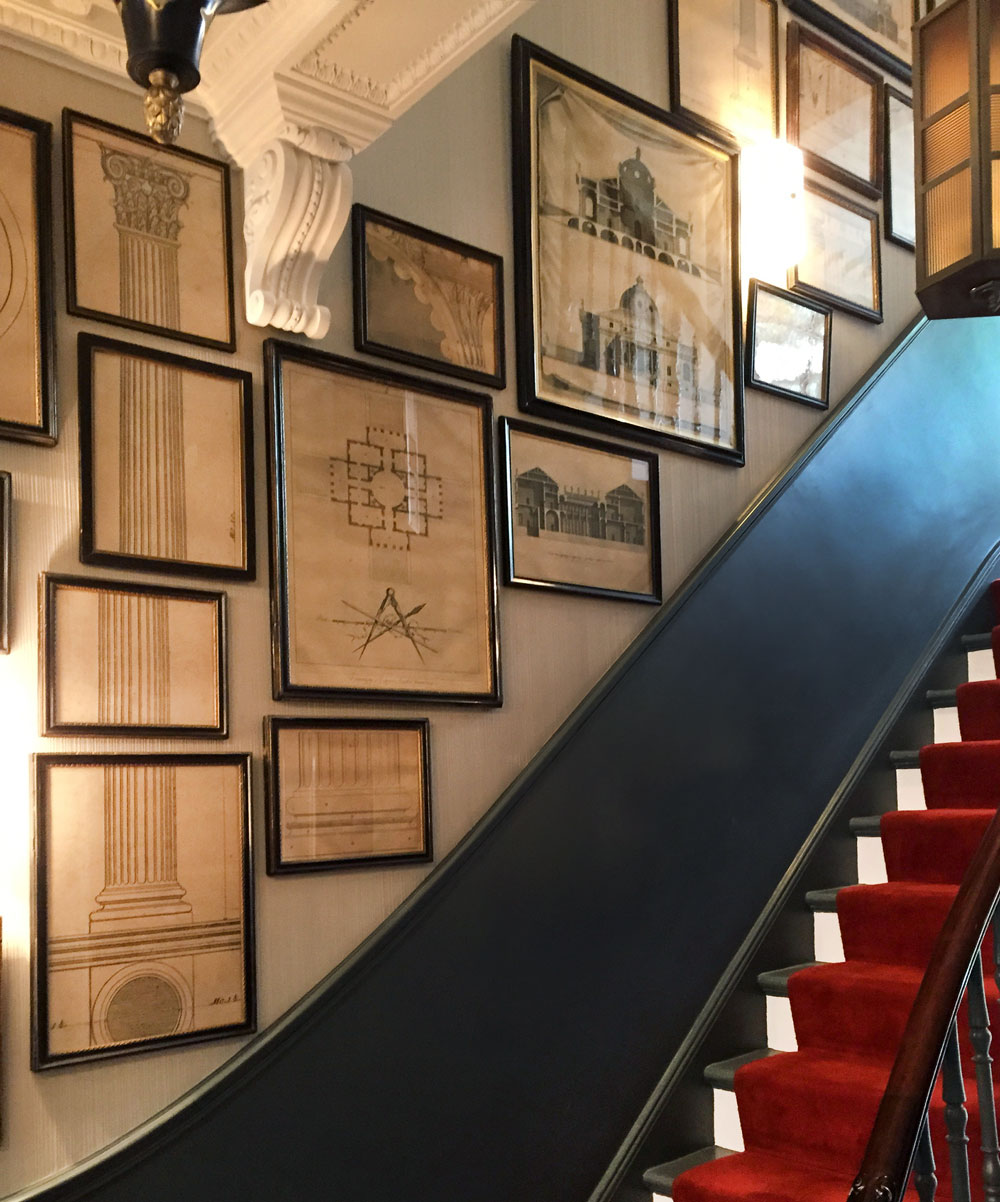 The staircase is framed with many Piranesi architectural drawings. A large pillar is split across 4 frames to form the whole image. Architect schemes and drawings of buildings are hung along the walls.