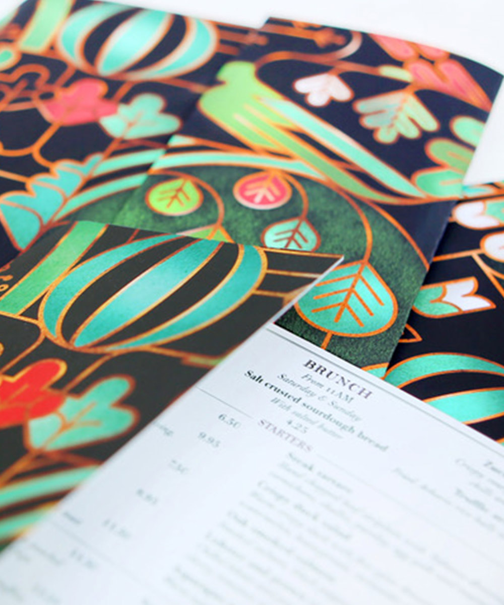 A menu cover design for The Ivy City garden showing intricate pattern includes birds, botanicals and graphic shapes outlined in burnished brass colours.