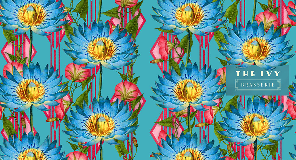 Blue lily flowers create a graphic pattern against pink diamond shapes. A pink flowered botanical vine weaves amongst the flowers.