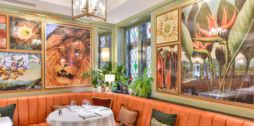 Framed contemporary artwork fills the panelling about the banquette seating. Artwork contains a large lion face, mixed botanicals, and academic professors in graduation ceremony dress.