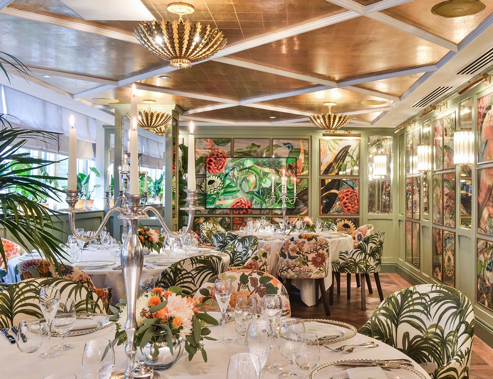 Framed oversized toucans fill the floor to ceiling panelling in the private dining room. A television sits amongst the frames and continues the artwork seamlessly across the screen. The tables are set for a high end dinner service.