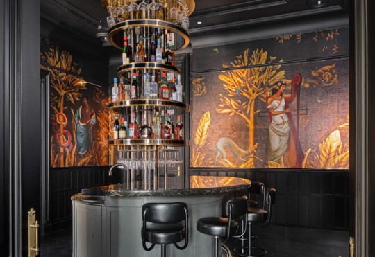 Black and gold metallic wallpaper surrounding bar area. Design features historical hungarian figures and animals amongst a grove of golden trees
